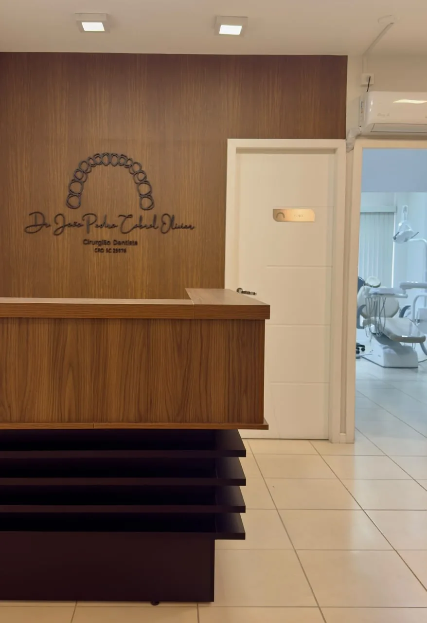 Recepção do consultório do Dr. João Pedro Cabral Olivier, com balcão de madeira e logotipo na parede